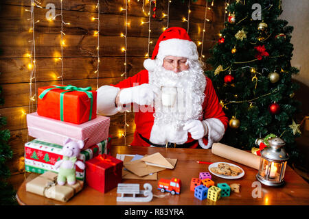 Frohe Weihnachten und schöne Feiertage. Santa Clause bereitet Geschenke für Kinder zu Weihnachten am Schreibtisch zu Hause. Stockfoto