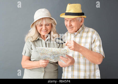 Ältere Touristen in Strand hüte Studio stehen isoliert auf grau auf Karte über Lupe heiter Stockfoto