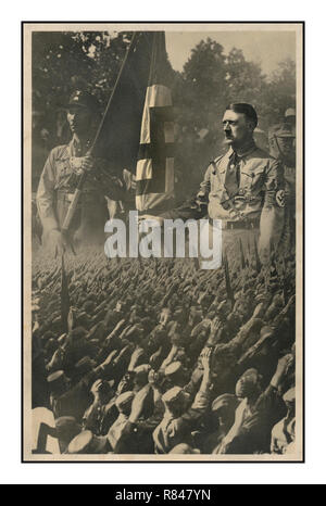 Jahrgang 1930 Die NS-Propaganda Postkarte zeigt eine Masse der ehrenkompanie Deutschen auf ein vergrößertes Bild von Adolf Hitler mit einem Mitglied der SA (Storm Trooper) Wer hält eine Hakenkreuzfahne überlagert. München, Deutschland, c 1933 von Hoffmann, Hitlers persönlicher Fotograf... SA, Abkürzung für Sturmabteilung (Deutsch: "Assault Division"), beinamen Sturmtruppen oder Braunhemden, Deutsche Sturmtruppen oder Braunhemden, in der deutschen nationalsozialistischen Partei, einer paramilitärischen Organisation, deren Methoden der gewaltsamen Einschüchterungen eine Schlüsselrolle in Adolf Hitlers Aufstieg zur Macht gespielt. Stockfoto