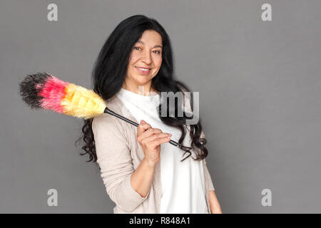Freestyle. Reife Lady stehen isoliert auf Grau mit Duster lächelnd verspielt Stockfoto