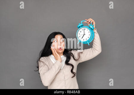 Freestyle. Reife Lady stehen isoliert auf Grau mit Wecker bis zum Zeitpunkt geschockt Stockfoto