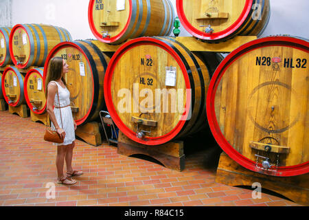 Junge Frau in einem Weingut in Montalcino, Val d'Orcia, Toskana, Italien neben Holzfässern. Montalcino ist berühmt für seinen Brunello di Montalcin Stockfoto