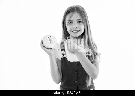 Mädchen mit grossen Lächeln holding Donut. Animierte Dessert, verglaste Bagel mit Augen. Kid zeigen auf süsses, süsses Himmel. Kind mit langem Haar zu tragen rosa Outfit auf weißem Hintergrund. Stockfoto