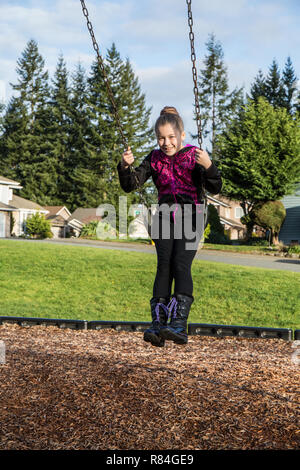 Issaquah, Washington, USA. Zehn Jahre altes Mädchen auf einer Schaukel sitzend auf einem Spielplatz. (MR) Stockfoto