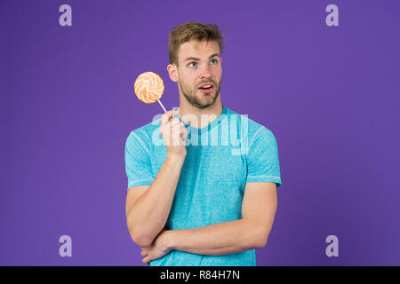 Cheat meal Konzept. Zucker schädlich für die Gesundheit. Kerl halten Lollipop candy violett unterlegt. Mann schöner macho Essen großen bunten süßen Lutscher. Geschmack der Kindheit. Mann mit Borsten mag Lollipop. Stockfoto