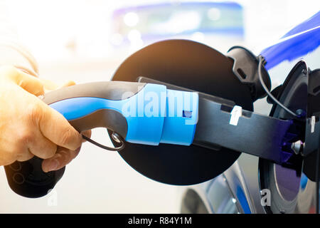 Man einschalten Laden von Auto. EV Auto oder Elektroauto an der Ladestation mit Netzkabel Netzteil in unscharfer Natur mit sanften Licht ba angeschlossen Stockfoto