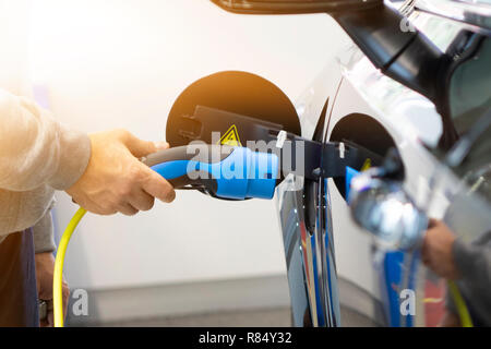 Man einschalten Laden von Auto. EV Auto oder Elektroauto an der Ladestation mit Netzkabel Netzteil in unscharfer Natur mit sanften Licht ba angeschlossen Stockfoto