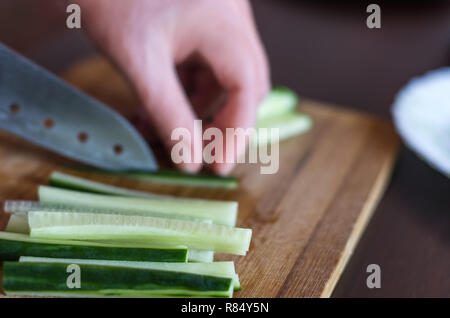 Die Frau Hände Schneiden Gurke Streichhölzer mit Santoku Messer auf einer hölzernen Schneidebrett. Salate, Maki, Temaki Sushi Rollen Zutat Stockfoto