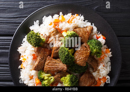 Gebratenen Rindfleisch Brokkoli mit Reis und persimmon Beilage close-up auf einem Teller auf den Tisch. horizontal oben Ansicht von oben Stockfoto