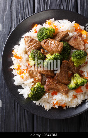 Gebratenen Rindfleisch Brokkoli mit Reis und persimmon Beilage close-up auf einem Teller auf den Tisch. Vertikal oben Ansicht von oben Stockfoto