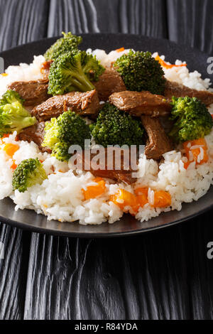 Gebratenen Rindfleisch Brokkoli mit Reis und persimmon Beilage close-up auf einem Teller auf den Tisch. Vertikale Stockfoto