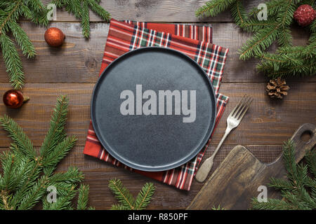 Weihnachten Lebensmittel Grenze mit schwarze Platte, evegreen Zweige, und rote Einrichtung auf Holzbrett. Platz für Text. Ansicht von oben.. Stockfoto