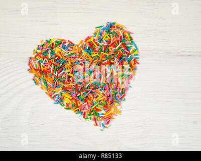 Candy besprüht Form Herz Form. Bunte Herz-Form von candy Konfetti auf weißem Holz- Hintergrund. Valentines Tag Konzept. Top View oder flach Stockfoto
