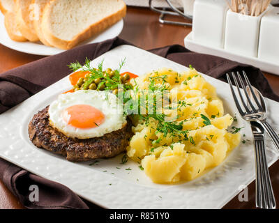 Beefsteak mit Spiegelei und Kartoffelpüree auf weiße Platte close-up auf dunkelbraunen hölzernen Tisch im Restaurant Stockfoto