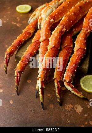 Frische leckere König Kamtschatka Crab Claw mit Zitronenscheiben auf Holz Brett an der braunen Hintergrund Stockfoto