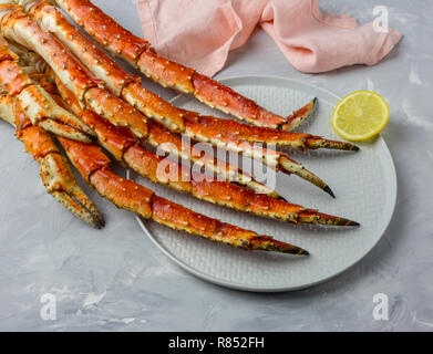Luxury Kamtschatka Crab Claw auf graue Platte mit Zitronenscheibe und rosa Serviette auf grauem Hintergrund Stockfoto