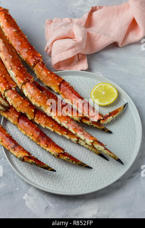 Luxury Kamtschatka Crab Claw auf graue Platte mit Zitronenscheibe und rosa Serviette auf grauem Hintergrund Stockfoto