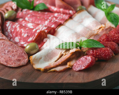 Antipasto set platter auf Holzplatte. Kalt geräucherte Fleisch Platte mit Wurst, Schinken, Schinken, Speck, Oliven und Basilikum. Vorspeise auf Holz Fach geschnittenen Baum gesägt Nachahmung. Platz kopieren Stockfoto