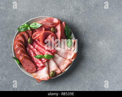 Antipasto set platter auf die Platte über der grauen Stein. Kalt geräucherte Fleisch Platte mit Wurst, Schinken, Schinken, Speck, Oliven und Basilikum. Vorspeise Sorte mit kopieren. Top View oder flach. Stockfoto