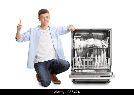 Junge Mann neben einem beladenen Spülmaschine mit Daumen oben auf weißem Hintergrund kniend Stockfoto