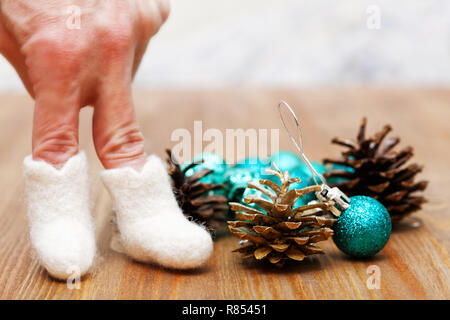 Weihnachten und neues Jahr Spielzeug Dekoration auf Holz- Hintergrund. Menschliche Finger in Spielzeug, Stiefel, Tannenzapfen und Grüne Weihnachten Kugeln. Flache konzentrieren. Stockfoto