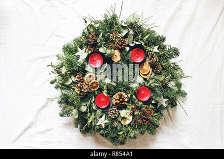 Weihnachten Adventskranz auf weißem Hintergrund. Durch immergrüne Tannenbaum Äste dekoriert, Eukalyptus Blätter, Holz- Sterne, Tannenzapfen, Beeren und rote Kerzen. Flach, Ansicht von oben. Stockfoto