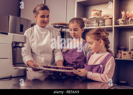 Bereit zum Backen. Angenehme nette Mädchen Holding ein Fach mit Muffins, während es in den Ofen Stockfoto