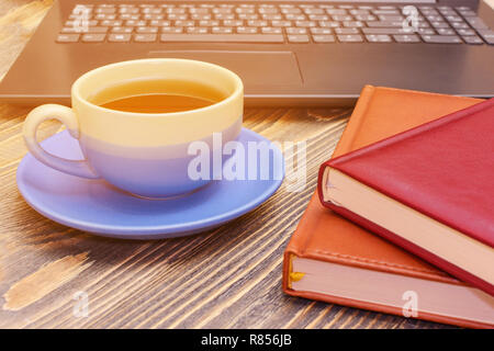 Eine Tasse Tee und zwei Notebooks mit einem Laptop auf einen hölzernen Tisch. Von der Seite. Kleine Tiefenschärfe. Stockfoto