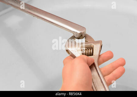 Der Filter für den Wasserhahn hand schraubt einen Schraubenschlüssel auf dem Hintergrund einer weißen Badewanne. Stockfoto