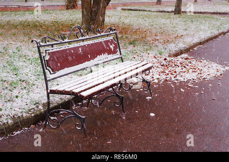 Herbstlandschaft: Alte Gartenbank im Spätherbst der erste Schnee bedeckt. Schießen im November. Stockfoto