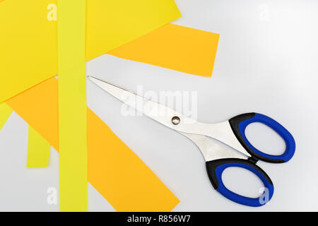 Scheren mit blauen Griffe an der weißen Neben den Schnitt farbiges Papier gelb und orange. Ansicht von oben. Stockfoto