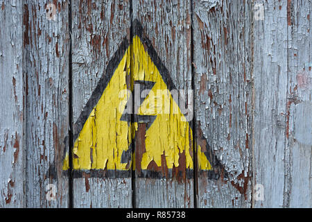 Alten rostigen Schild Gefahr Hochspannung auf eine Holzwand mit Blätterte von weißer Farbe. Stockfoto