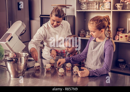 Cupcake master class. Positive Konditor mit ihr Schüler und zeigt wie Cupcakes dekorieren Stockfoto