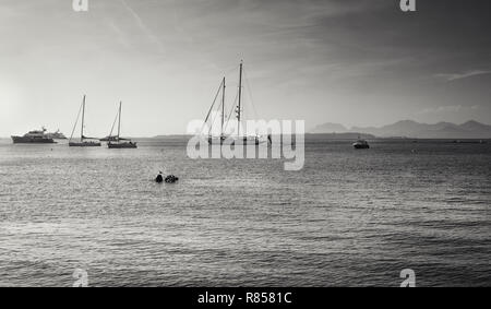 Schwarz-weiß Bild der Yachten und Segelboote vor Anker in Golfe Juan im Beach Resort in Juan-les-Pins mit der Insel Ile Sainte-Marguerite Stockfoto