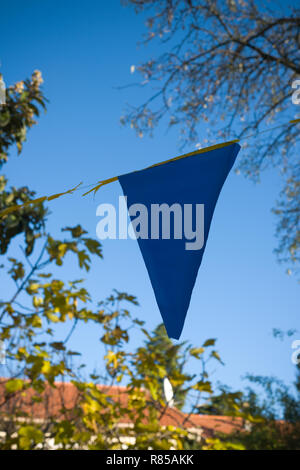 Auf der Suche auf ein Dreieck aus einem bunting Linie gegen einen strahlend blauen Himmel, die über einen Garten mit Haus Dach und Bäumen Stockfoto