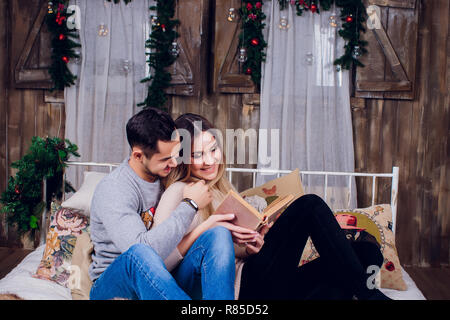 Die schöne Zeit zu Hause. Schöne junge Liebende Paar kleben aneinander und lächelnd, während Frau mit einem Buch. Stockfoto