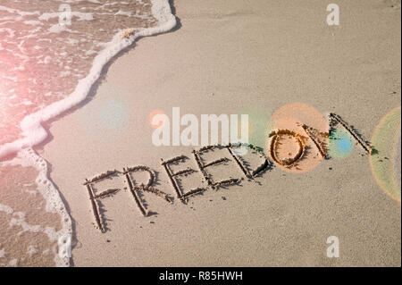 Freiheit Nachricht handschriftlich in sanften Sand mit inspirierenden lens flare Neben entgegenkommende Welle Stockfoto