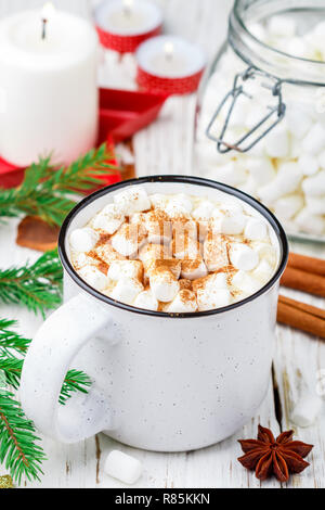 Heißer Kakao (Kaffee oder Schokolade) mit Marshmallows und Zimt in eine weiße Schale. Süßigkeiten, Kerzen und Tannenzweigen auf dem Tisch. Weihnachten. Für das neue Jahr. Rost Stockfoto