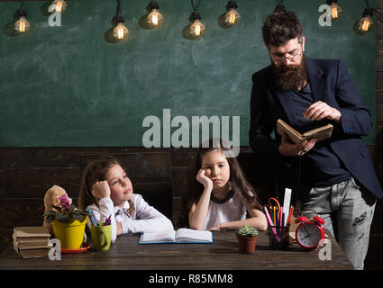 Langweilig Lektion Konzept. Mann mit Bart unterrichtet Schülerinnen, Buch zu lesen. Gelangweilt und müde Kinder hören Lehrer. Lehrer und Schüler Mädchen im Klassenzimmer, schwarzes Brett für den Hintergrund. Stockfoto