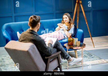 Junge Frau, die in der männlichen Psychologen liegen auf der bequemen Couch bei tiefenpsychologischen Sitzung in der Luxury blue Office Interior Stockfoto