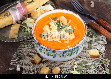 Kürbispüree Suppe mit Crackern, Baguette und Schinken auf hölzernen Tisch Stockfoto