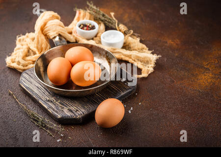 Hühner braune Eier und eine kleine Skillet - ein Satz für das Rührei oder Omelett, Salz und Gewürze auf einem braunen Hintergrund Stockfoto