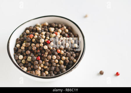 Verschiedene Arten von Pfeffer Samen in einer weißen Schüssel auf einem weißen Hintergrund. Makro Fotografie. Stockfoto