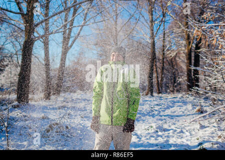 Junger Mann Schnee werfen im Winter Wald. Kerl Spaß im Freien. Man Frieren unter fallenden Schnee. Aktivitäten im Winter. Stockfoto