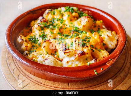 Gebackener Blumenkohl Käse gemacht mit Red Leicester serviert in einem rustikalen rot Keramik runde Schale. Mit einem Gratin top gekocht und mit Petersilie bestreut. Die d Stockfoto