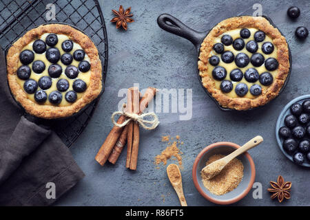 Leckere Heidelbeeren Törtchen mit Vanillepudding Creme auf dunkel strukturierten Hintergrund. Ansicht von oben, flach Stockfoto