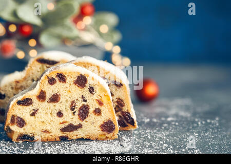 Christstollen auf blau-grünen Hintergrund mit festlichen Weihnachtsbeleuchtung und roten Beeren im Winter, kopieren - Raum. Traditionelle deutsche Dessert für Weihnachten celeb Stockfoto