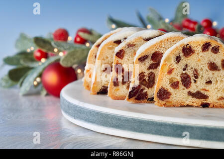 Christstollen auf Weiß-Blau festliche Hintergrund mit Beeren und Weihnachtsbeleuchtung. Traditionelle deutsche Dessert für Weihnachten feiern. Stockfoto