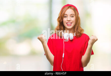 Junge schöne hipster Frau über isolierte Hintergrund das Tragen von Kopfhörern und Kappe überrascht Feiern und für den Erfolg mit erhobenen Armen und Op erstaunt Stockfoto