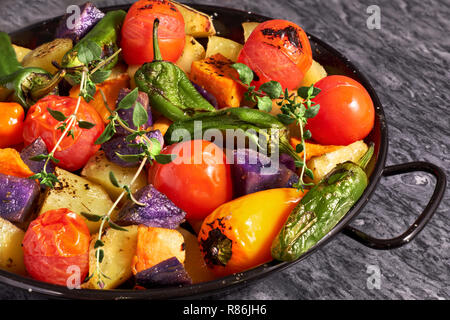 Rustikalen Ofen gebackenes Gemüse in schwarz Auflaufform con grauen Stein Hintergrund. Saisonale vegetarische vegane Mahlzeit. Zutaten: Kartoffeln, Lila und süßen p Stockfoto